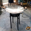 Fogão a gás com chapa metálica marmorizada em formato flor, com pega de madeira, em ambiente de oficina