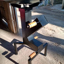 Suporte preto metálico com três manípulos de madeira e ambiente externo com chão de terra