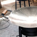 Grelha redonda em metal com borda ondulada e alça com detalhe em cobre, ambiente de cozinha industrial