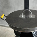 Chapa de ferro grande com tampa e alça amarela, usada para culinária em fogão a lenha