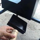 Mão segurando alça de madeira em porta giratória de chapa preta, coletando cinzas em bandeja