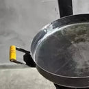 Frigideira de ferro com alça amarela sobre superfície cinza desfocada