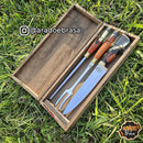 Conjunto de faca, garfo e chaira com cabo de madeira em caixa artesanal sobre grama verde